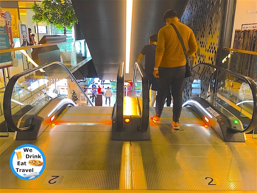 View of escalators in Gaysorn Village Bangkok with people stepping on to go down to the next level.