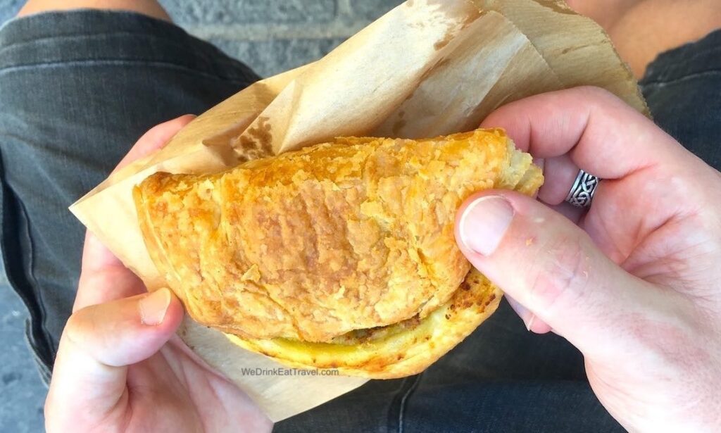 Close-up of a ricotta pastizzi in Malta, with golden pastry being held on a brown paper bag.