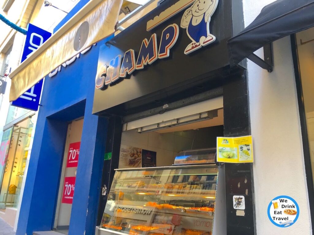 Open shopfront for Champ Pastizzeria in Malta showcasing a variety of food in clear display cabinets and signs with pictures showing different food on offer.