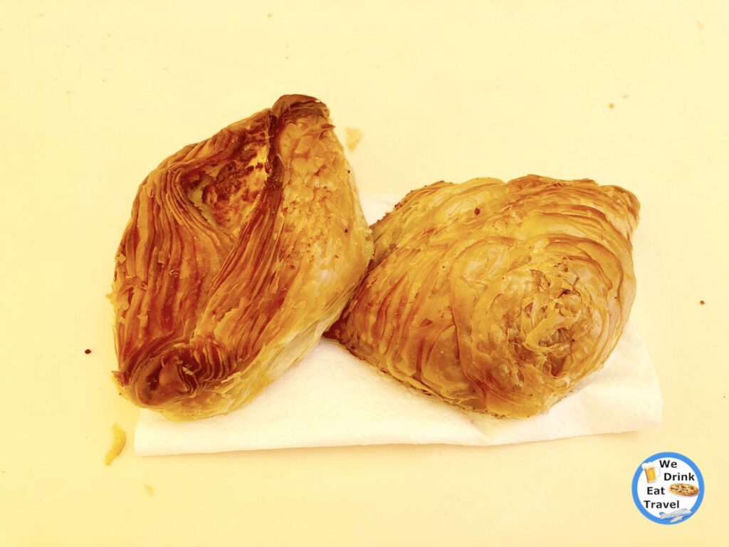 Delicious traditional Malta food, with a close-up of 2 different pastizzis with delicate layers of deep golden flaky pastry on a white paper serviette.