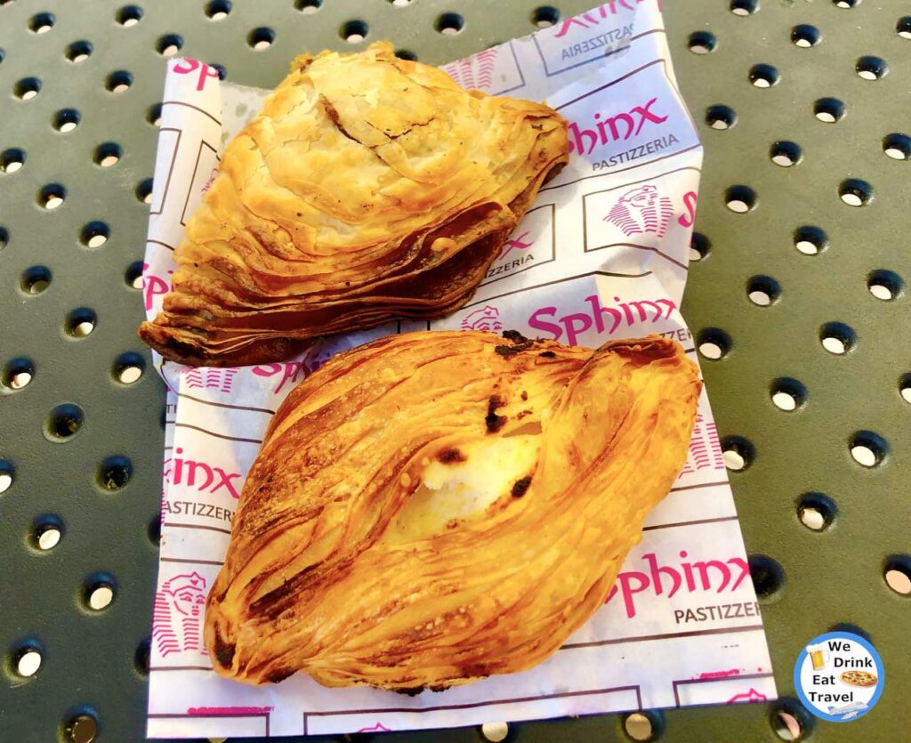 Close-up of 2 different pastizzis from Sphinx Pastizzeria in Malta, with layers of deep golden flaky pastry on a branded paper bag.