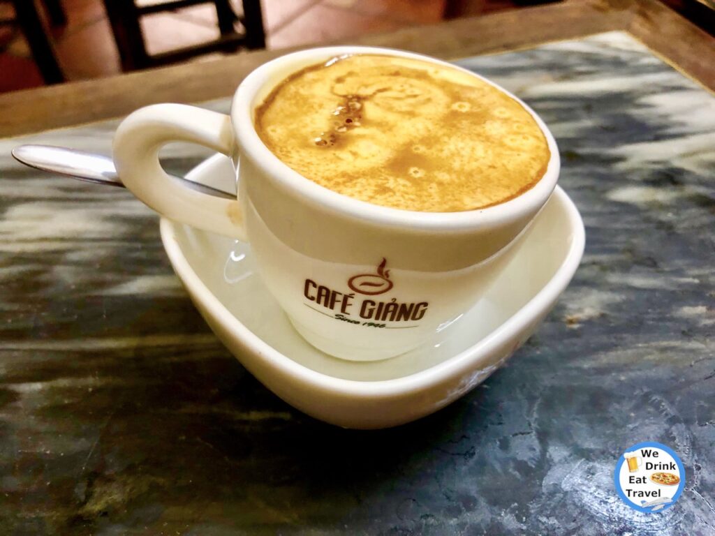Close-up of a Vietnamese egg coffee at Cafe Giang Hanoi, showcasing the coffee in a white porcelain cup, floating in a small bowl of water.