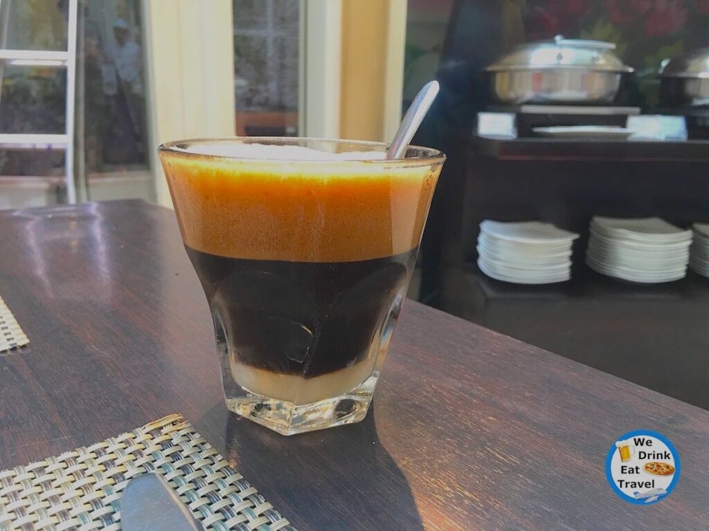 Close-up of the Vietnamese coffee ca phe sua with condensed milk at the bottom of the glass, rich dark coffee and the foam on top.