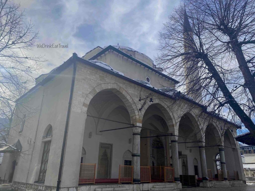 The historic Gazi Husrev-beg Mosque in Sarajevo, featuring a tall white minaret and traditional stone domes.