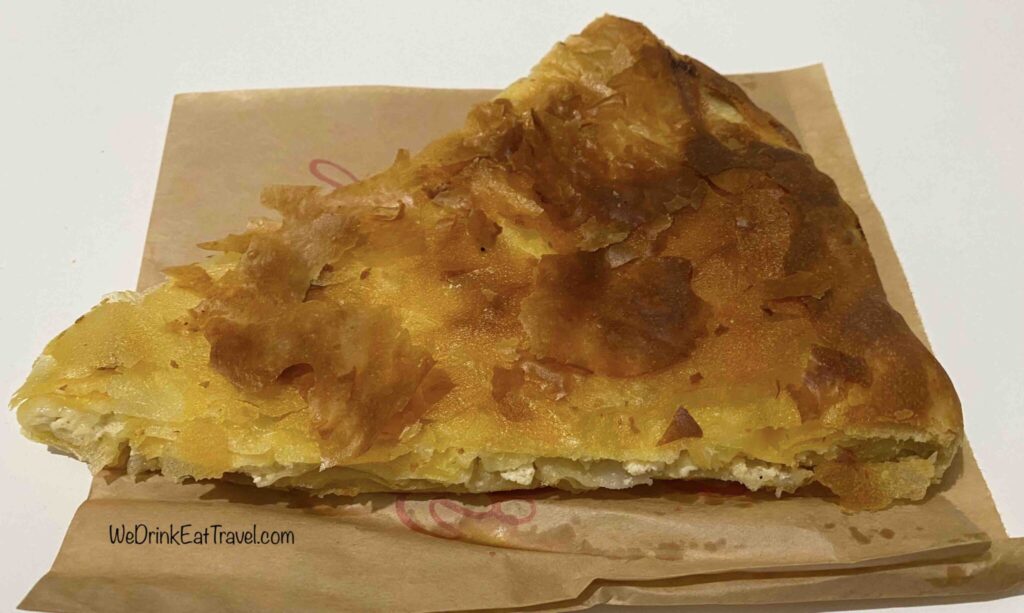 Close-up of an Albanian byrek with golden flaky pastry and white cheese between layers of pastry on a brown paper bag.