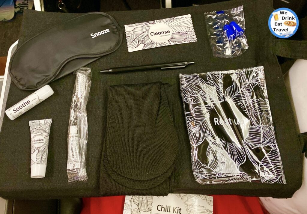 Amenity kit on a Jetstar Business Class flight including silk eye-shades, lip balm, hand cream, toothbrush and toothpaste set, black socks, a pen, blue earplugs, and inflatable neck pillow.