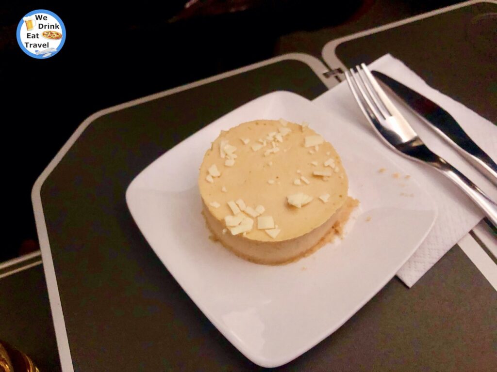 A dessert on a Jetstar Business Class flight showcasing a caramel mousse with shards of crushed white chocolate on a plate with cutlery and serviette.