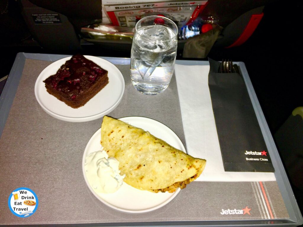 Food on board a Jetstar Business Class flight from Bangkok to Melbourne showing a chocolate brownie and a filled tortilla with cream cheese on the side, water and cutlery.
