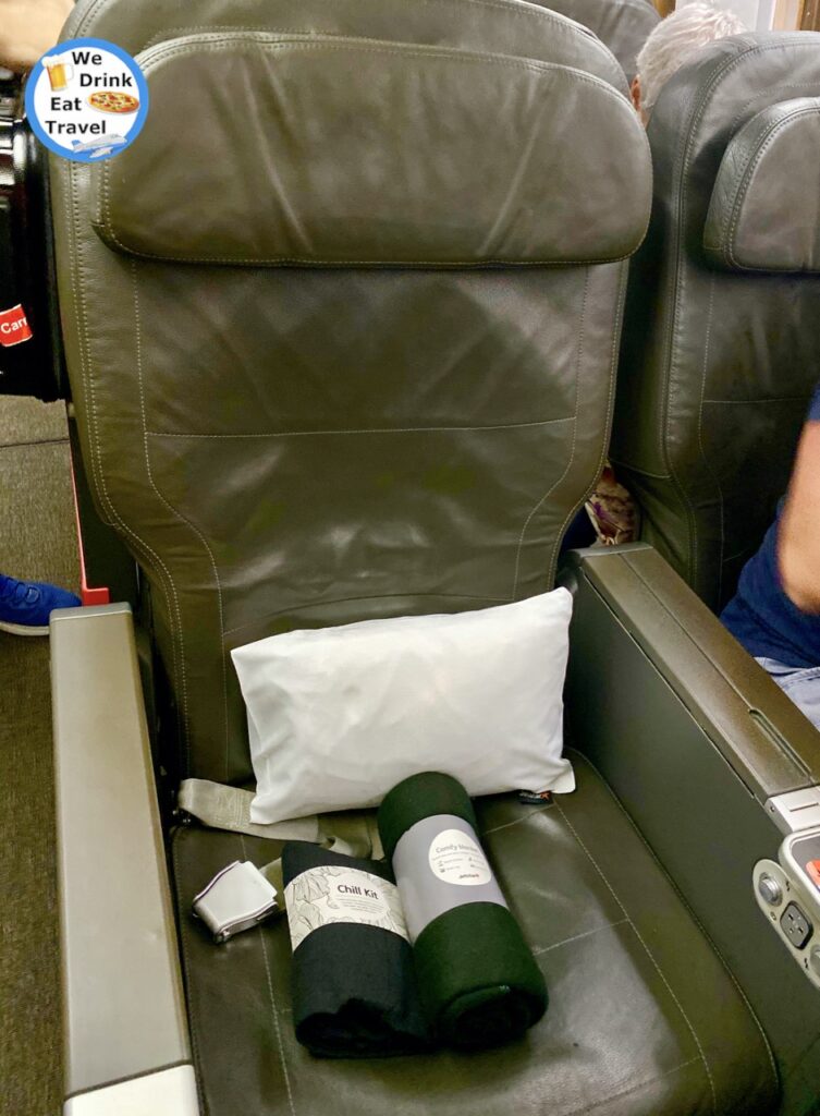 A Jetstar business class seat with a leather-look covering, and on the seat is a small white pillow, a chill kit and comfy blanket.