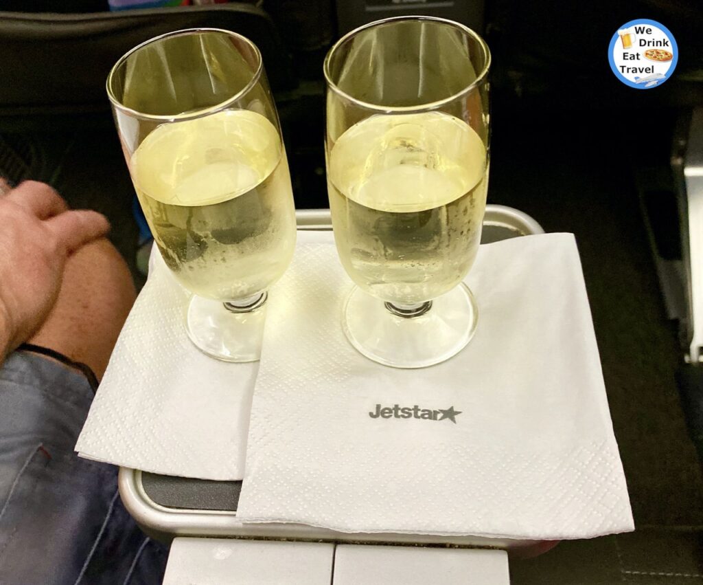 Close-up of 2 glasses of sparkling wine on board a Jetstar business class flight with 2 white serviettes beneath with the brand on it.