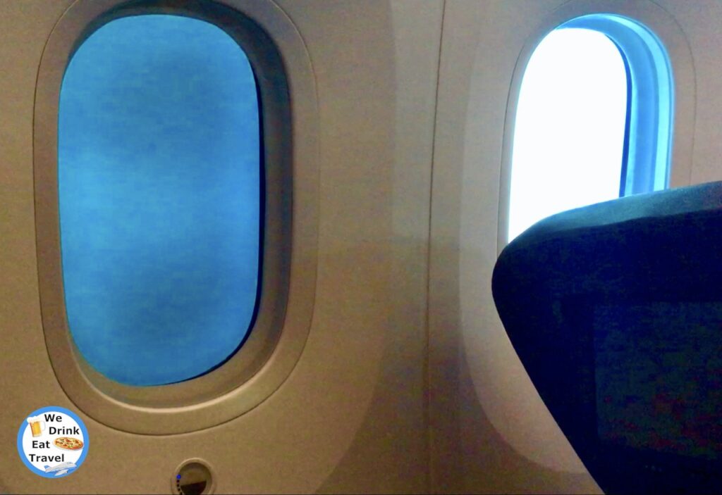 Windows on a Jetstar business class flight from Bangkok to Melbourne with one shade open and the other shade closed.