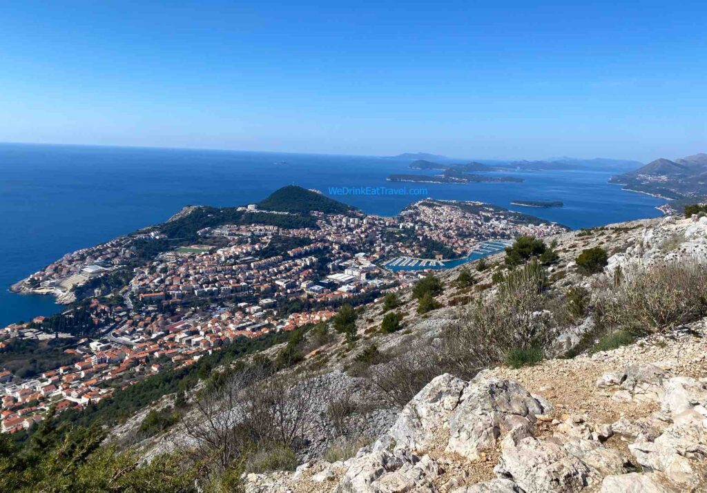 Panoramic view of Dubrovnik, Croatia, from Mount Srđ, showcasing the terracotta rooftops of the Old Town, the Adriatic Sea, and surrounding islands under a clear blue sky.