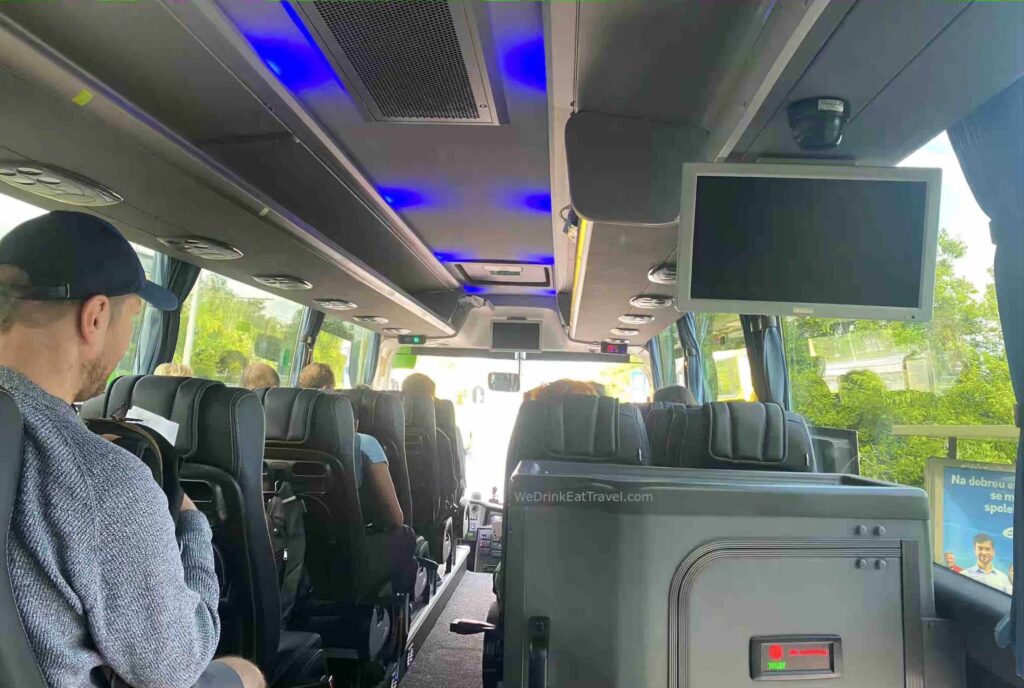 Interior view of a Flixbus tour bus with passengers seated, featuring blue LED lighting overhead, screens for entertainment, large windows and curtains.