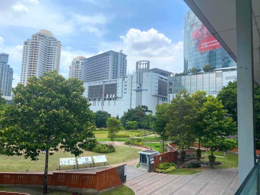 View of Platinum Fashion Mall in Bangkok from the Ratchaprasong Skywalk with a lush green park with trees in the forefront.