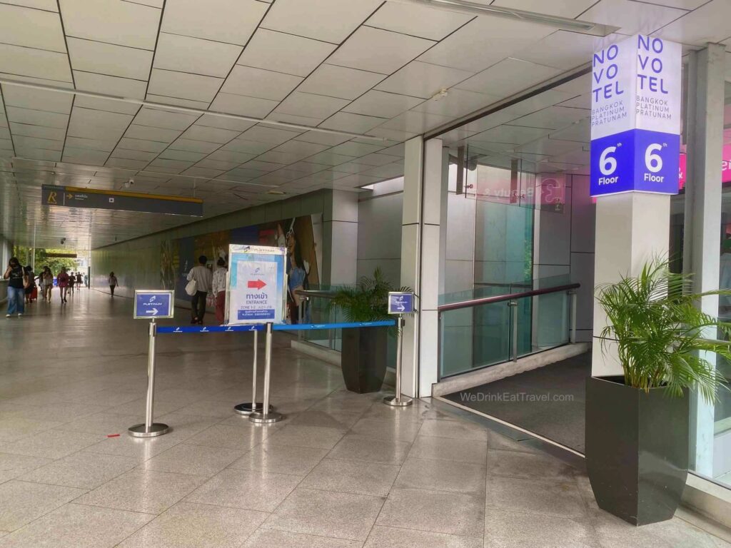Entrance to Platinum Fashion Mall in Bangkok for Zones 1 and 2, with people walking around the building in the background.