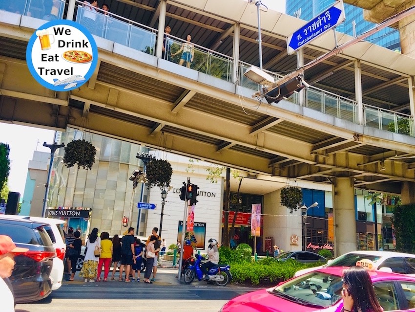 Pedestrian walkway above Ratchadamri Road in Bangkok with Gaysorn Shopping Centre in the background. Pedestrians, motorbikes and traffic pass by on the roads.